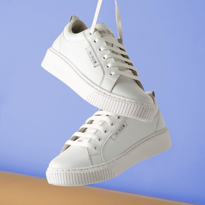 Example photo: Pair of white leather sneakers hanging by their laces against a blue backdrop