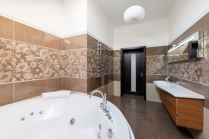 Example photo: Dated bathroom with brown patterned tiles, a corner jet tub and a wood vanity