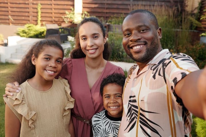 Example photo: Smiling family of four standing close together outdoors in daylight