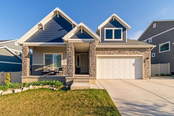 Example photo: Suburban house with stone columns, blue siding and a white garage in bright daylight