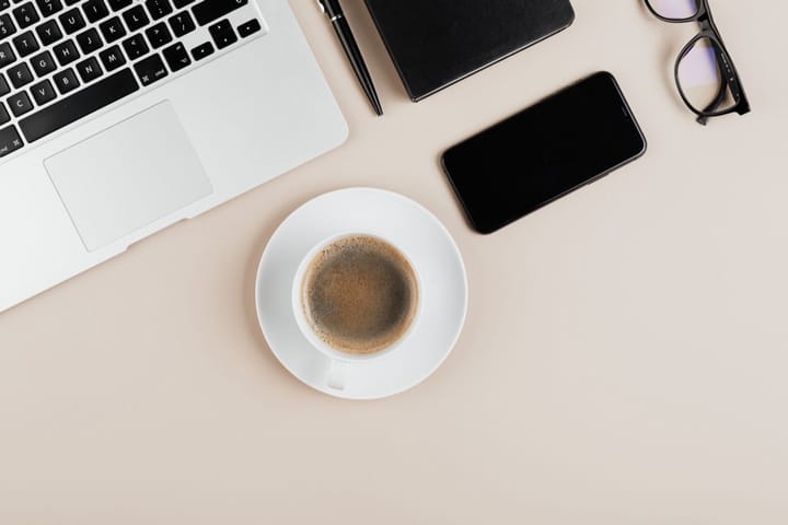 Example photo: Top-down desk with a laptop, coffee cup, phone and glasses, no people