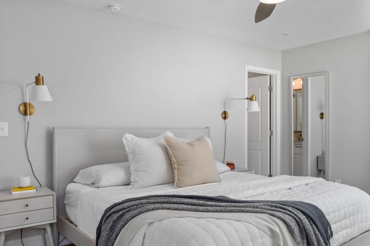 Example photo: Bedroom with light gray walls, brass wall sconces and a made bed